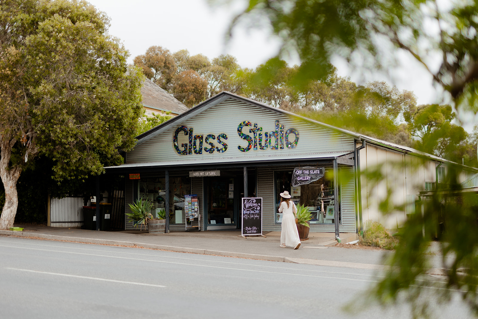 Female in a white dress and hat walking in to the glass studio in willunga