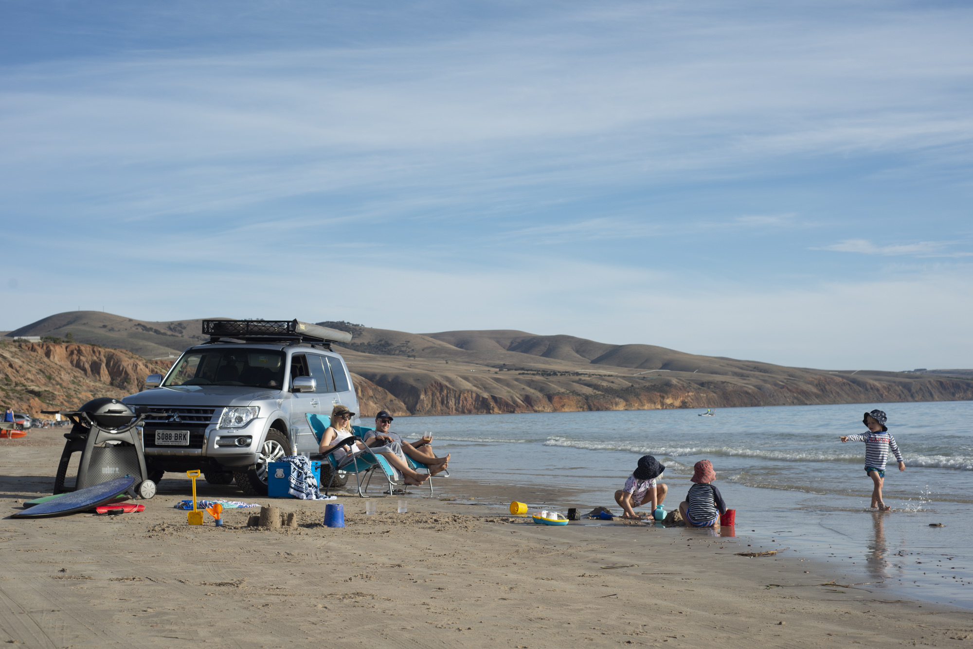 A group of people playing at the beach and some people standing around the car that is on the beach.