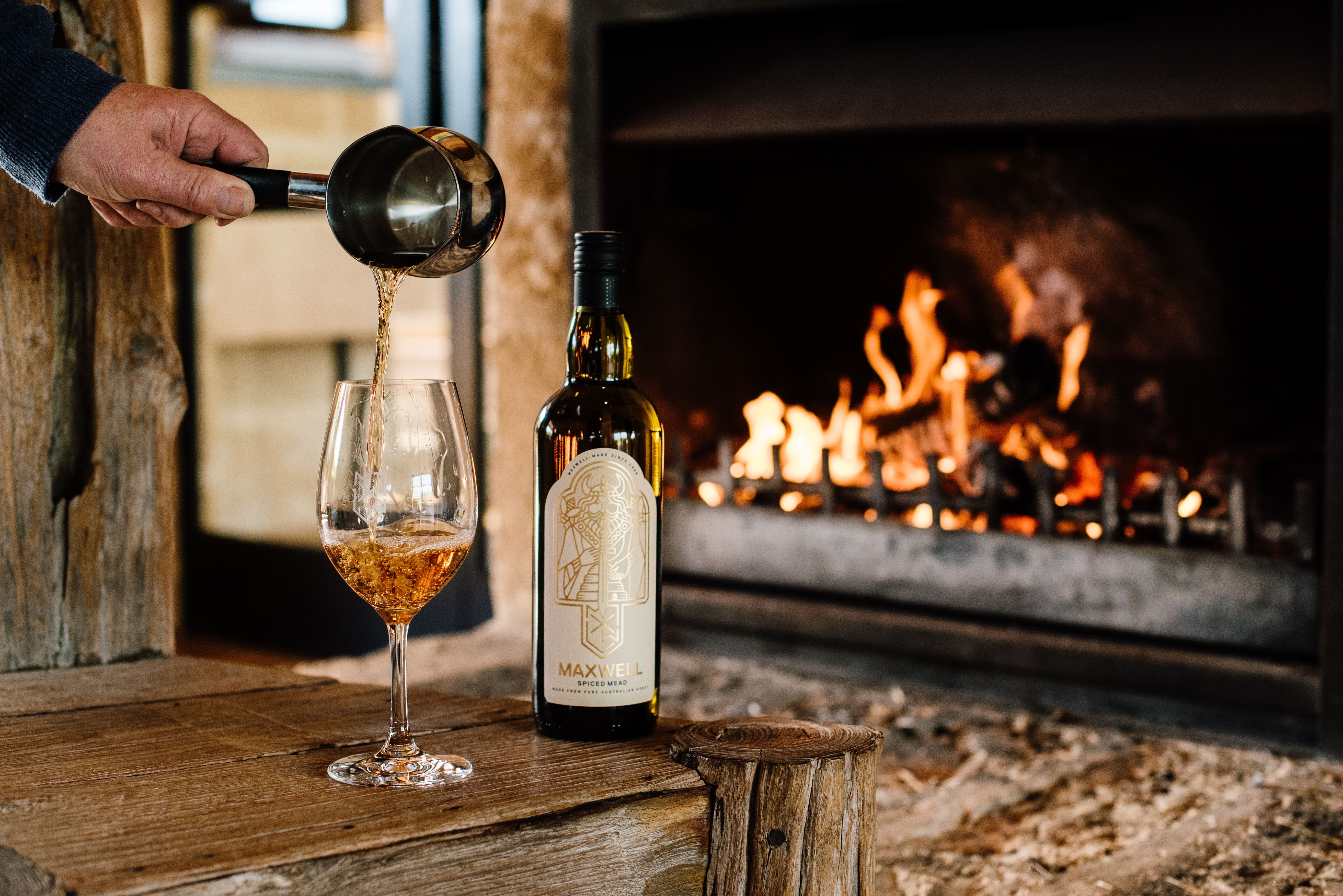 A bottle of whisky on a table in front of a fireplace with a glass