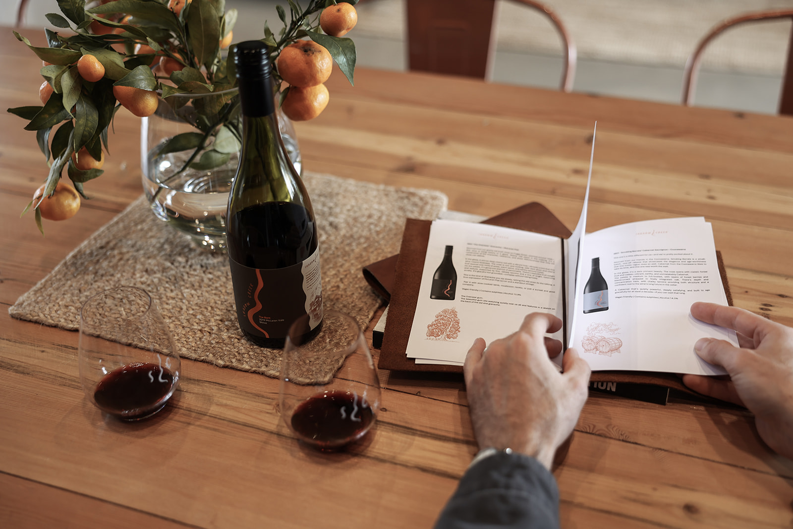 Two glasses on table with red wine and a bottle with a menu open