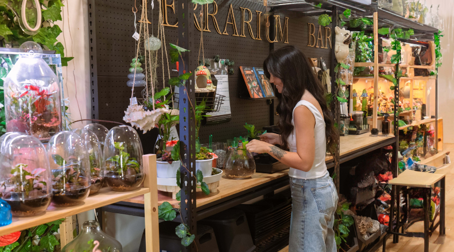 A woman building a terrarium at the Botanista Terrarium Bar in McLaren Vale, surrounded by glass domes, plants and miniature decorations